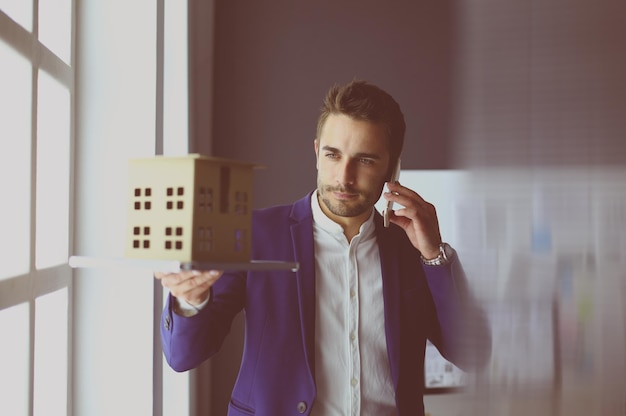 Foto empresário segurando a miniatura da casa na mão em pé no escritório