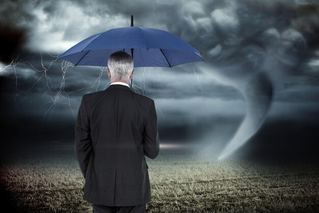 Empresário segurando guarda-chuva contra céu tempestuoso com tornado sobre campo