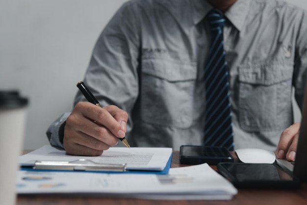 Empresário segurando o gráfico de documento de caneta contabilidade finanças papel análise gráfico investimento de marketing e economia de relatório com computador laptop na mesa no escritório