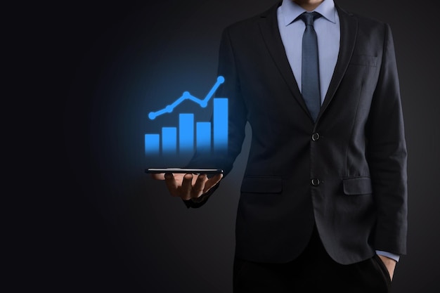 Empresário segurando o tablet e mostrando um holograma virtual crescente de gráfico de estatísticas e gráfico com seta para cima em fundo escuro mercado de ações planejamento de crescimento de negócios e conceito de estratégia