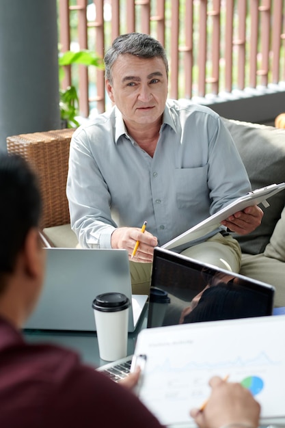 Empresario senior asistiendo a la reunión y discutiendo varios informes con colegas