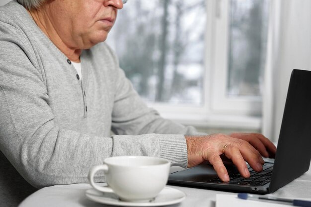 Empresário sênior de óculos sentado à mesa em frente ao laptop Homem mais velho bem-sucedido trabalhando em casa Cabelos grisalhos 60 anos 70 Homem ocupado digitando teclado olhando para o visor Escritório à distância