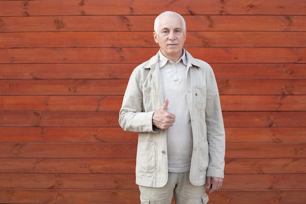 Foto empresario senior mostrando el pulgar hacia arriba sobre fondo de pared de madera