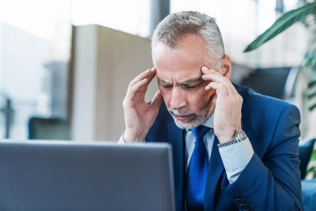 Empresario senior que siente dolor de cabeza mientras hace trabajo a distancia en una cafetería