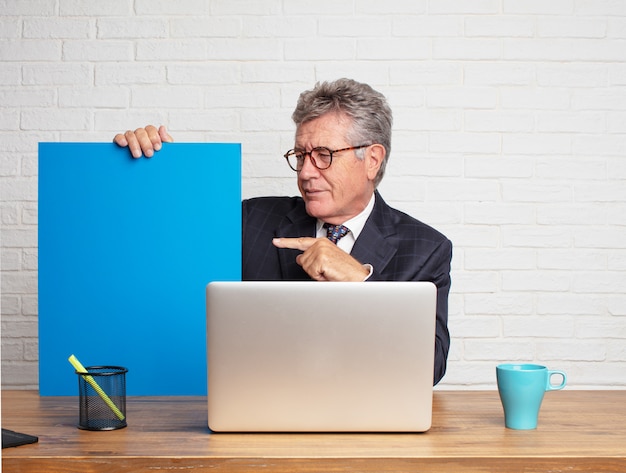 Empresario senior trabajando con su laptop y mostrando un vacío