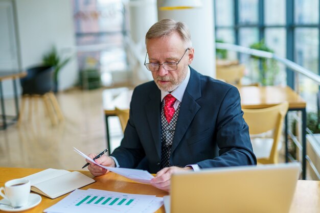 Empresário sentado à mesa com laptop lendo documento impresso