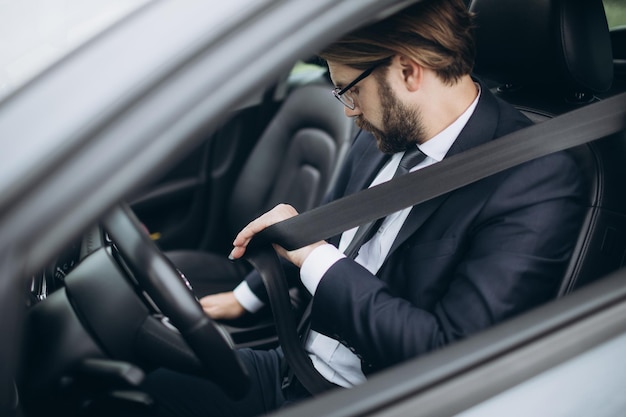 Empresario sentado en el auto y poniéndose el cinturón de seguridad