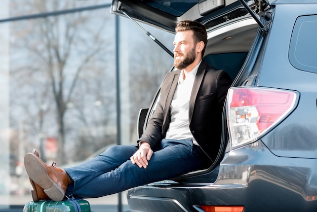 Empresário sentado com a mala no porta-malas do carro durante a viagem de negócios. conceito de viagem de negócios