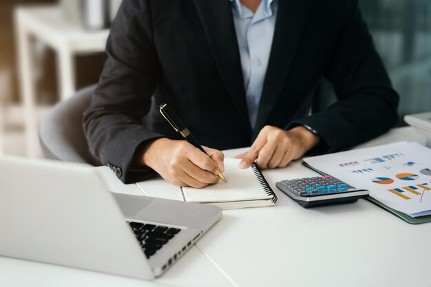 Empresário sentado em uma mesa em casa trabalhando em um laptop e anotando ideias em um caderno