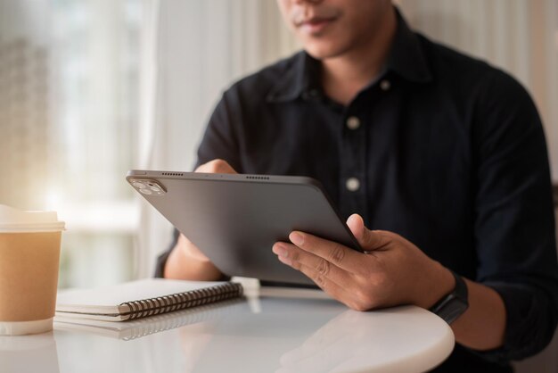 Empresário sentado em uma mesa em casa trabalhando em um laptop e anotando ideias em um caderno