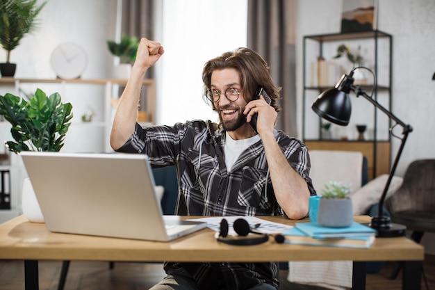 Foto empresario sentado en la mesa usando una computadora portátil moderna y un teléfono inteligente manteniendo el brazo levantado