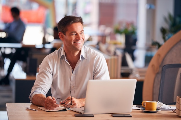 Empresário sentado na mesa escrevendo no notebook no escritório moderno de plano aberto