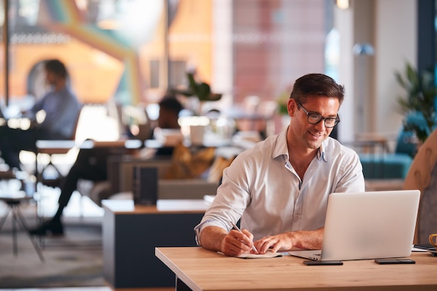 Empresário sentado na mesa escrevendo no notebook no escritório moderno de plano aberto