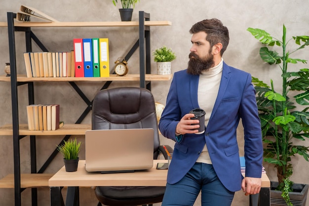 Empresário sério de terno bebendo chá ou café sentado no intervalo da mesa do escritório