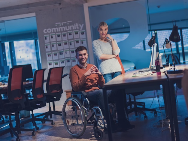 Foto empresario en silla de ruedas en un moderno espacio de oficina de coworking que trabaja tarde en la noche en la oficina. colegas en el fondo. concepto de discapacidad y minusvalía. enfoque selectivo