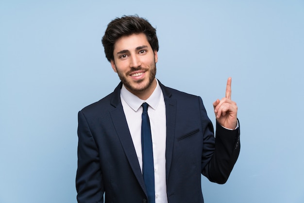 Empresario sobre una pared azul aislada que muestra y levanta un dedo en señal de lo mejor