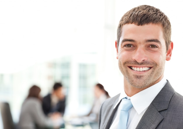 Empresario sonriendo a la cámara mientras su equipo está trabajando