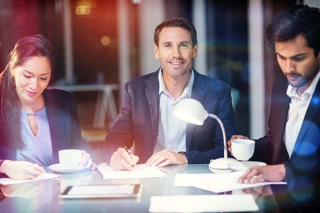 Empresario sonriendo mientras sus colegas escriben en papel