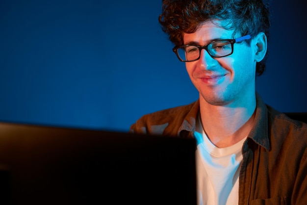 Empresario sonriente concentrándose en la computadora en un proyecto en la oficina de luz de neón Gusher