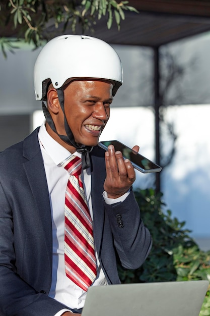 Empresario sonriente enviando un mensaje de voz mientras trabaja en una laptop sentada al aire libre