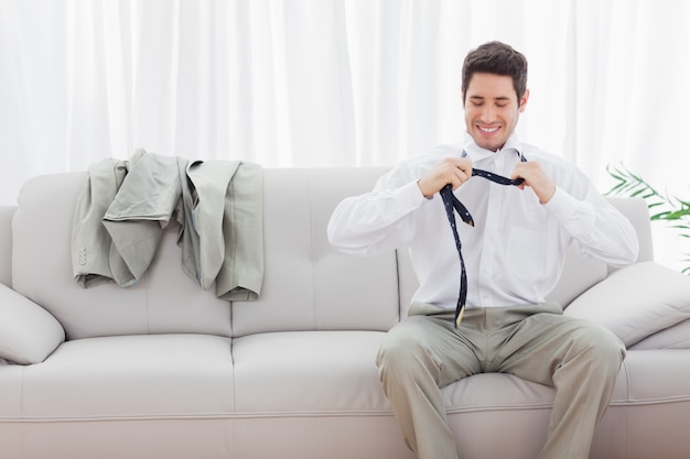 Empresario sonriente sentado en el sofá aflojando su corbata