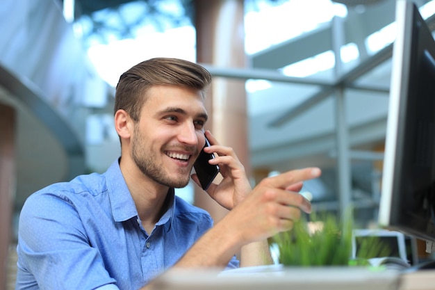 Empresario sonriente sentado y mediante teléfono móvil en la oficina