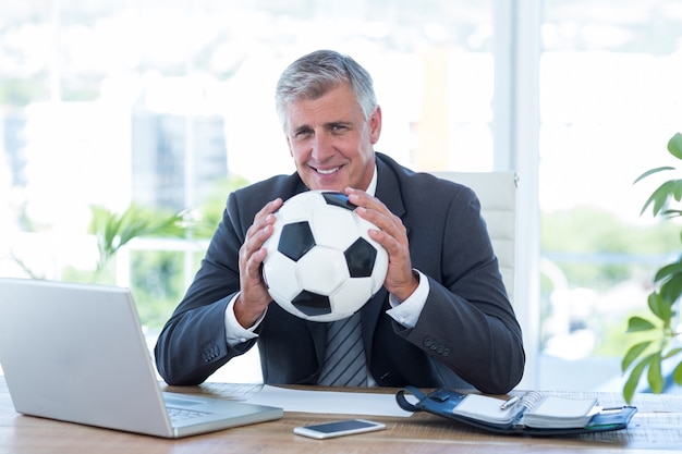 Empresario sonriente sosteniendo el balón de fútbol