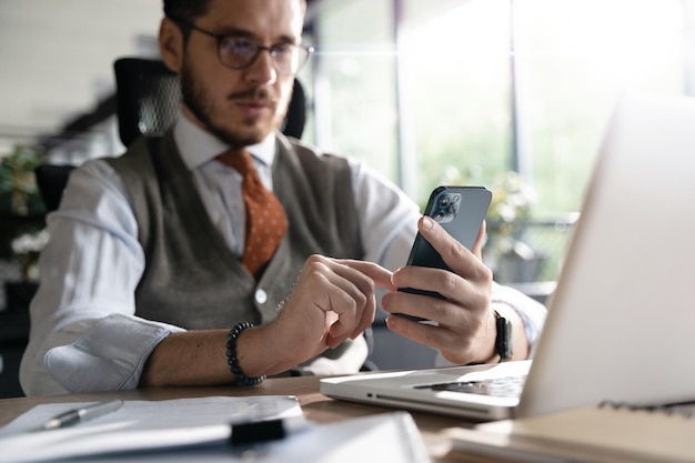 Empresario sonriente sosteniendo un teléfono inteligente sentado en la oficina Director ejecutivo de mediana edad usando aplicaciones móviles para teléfonos celulares