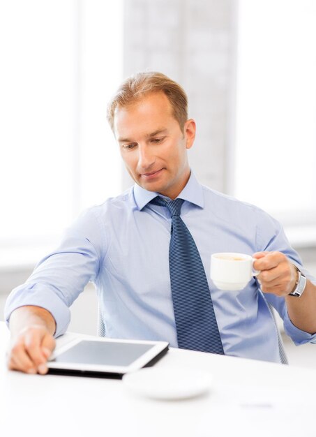 Empresario sonriente con tablet pc tomando café en la oficina