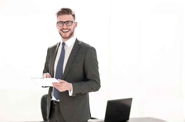 Empresario sonriente con tableta digital de pie cerca del escritorio