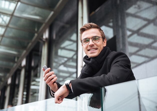 Empresario sonriente con teléfono cerca de la oficina