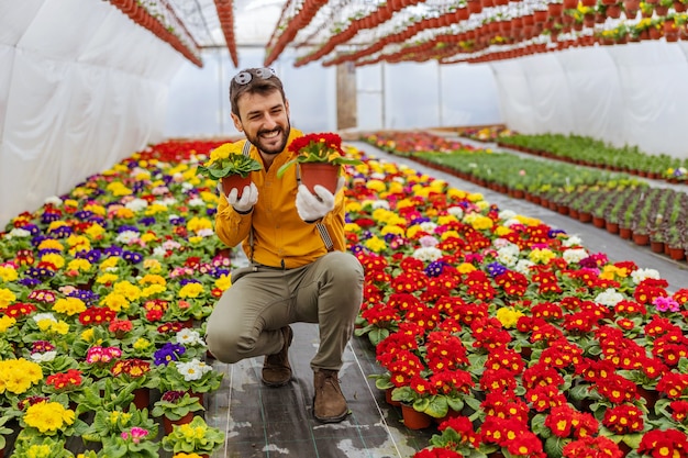 Empresário sorridente agachado em uma estufa e oferecendo flores como presente.