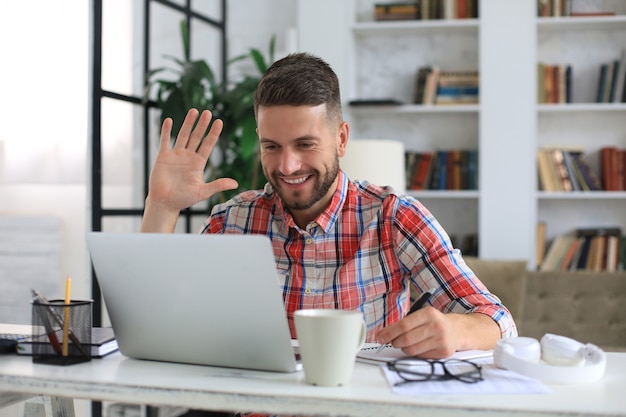 Empresário sorridente cumprimentando colegas em videoconferência e negociando à distância de casa.