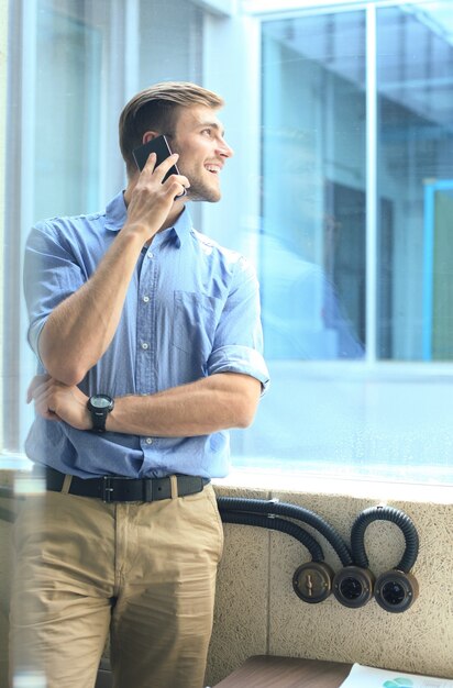 Empresário sorridente em pé e usando telefone celular no escritório