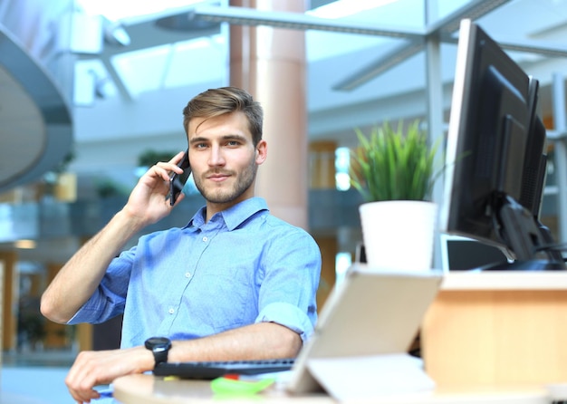 Empresário sorridente em pé e usando telefone celular no escritório