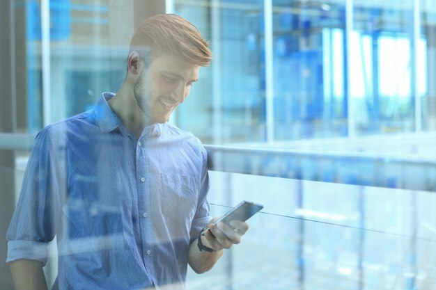 Empresário sorridente em pé e usando telefone celular no escritório