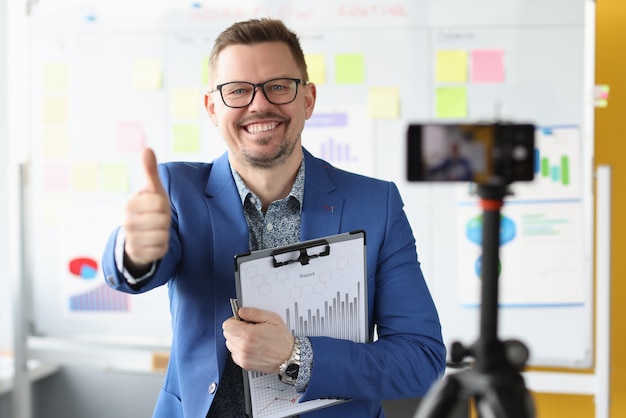 Empresário sorridente levanta o polegar e grava o treinamento empresarial em vídeo