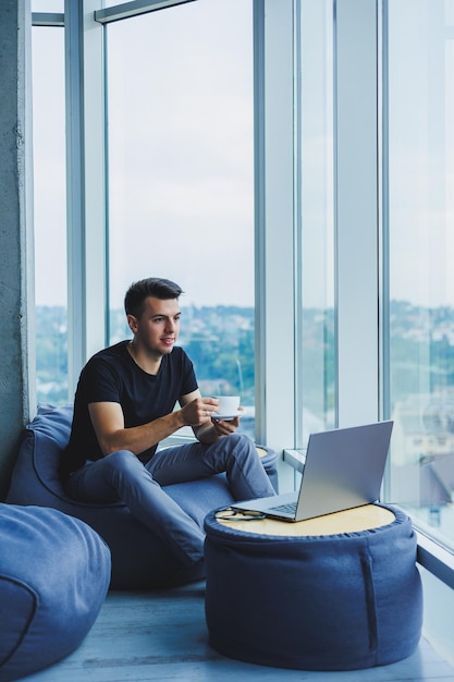 Empresário sorridente procurando algo e digitando em um laptop e bebendo café preto fresco O conceito de uma pessoa moderna e bem-sucedida Jovem focado com óculos em um escritório aberto