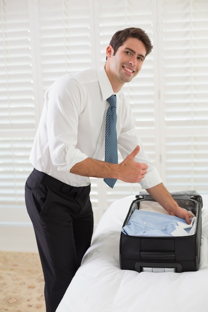 Empresário sorridente que desembala bagagem em um quarto de hotel