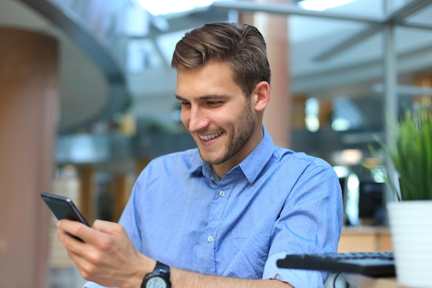 Empresário sorridente sentado e usando o celular no escritório