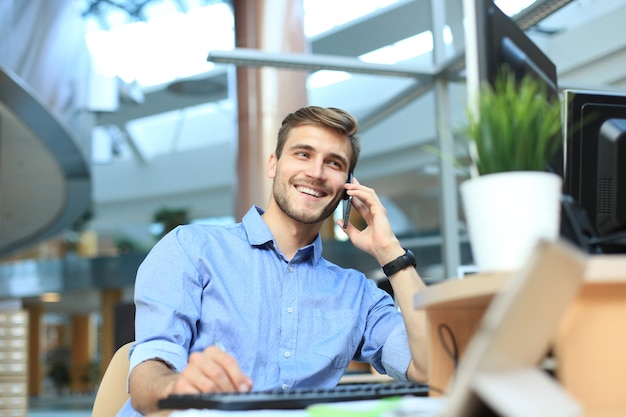 Empresário sorridente sentado e usando o telefone celular no escritório