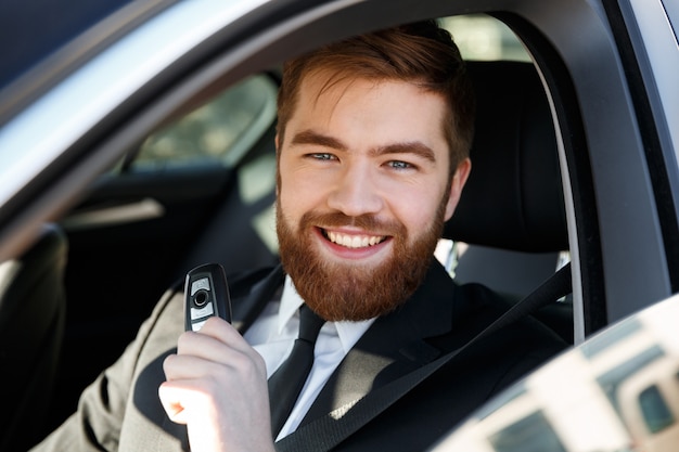 Empresário sorridente, sentado em um carro, mostrando as chaves do carro novo
