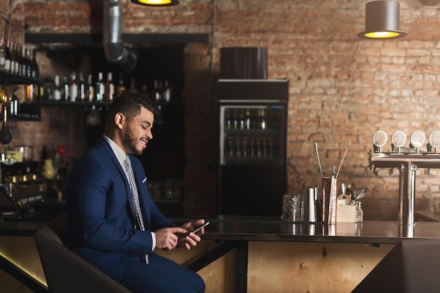 Empresário sorridente usando smartphone no bar, rede e se divertindo após um dia de trabalho árduo, copie o espaço