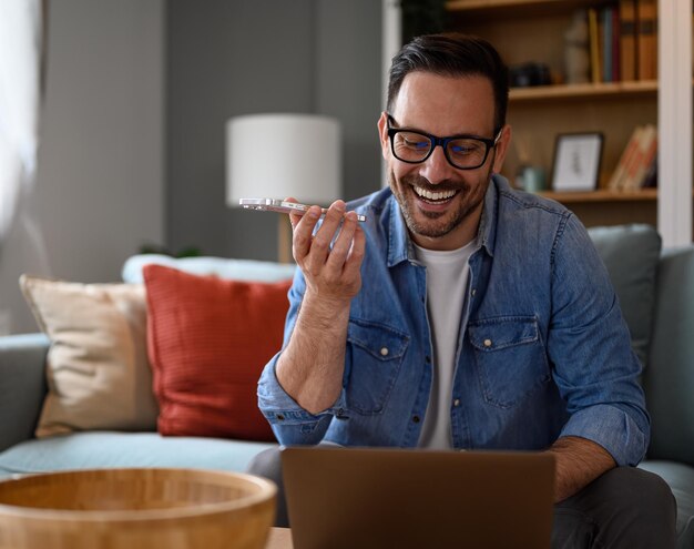 Foto empresário sorridente verificando e-mails sobre laptop e falando sobre telefone inteligente no escritório doméstico