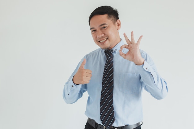 Empresário sorridente, vestindo camisa azul e gravata, posando com o polegar para cima e gesticulando bem sobre fundo branco