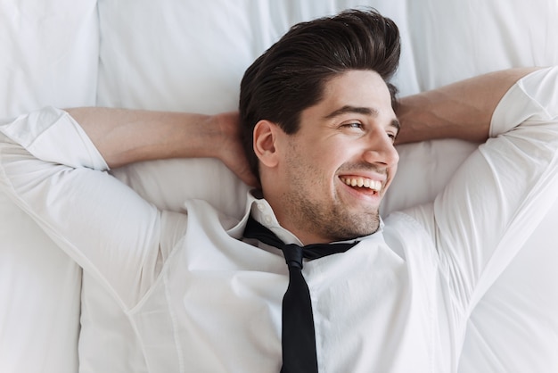 Foto empresário sorridente, vestindo roupas formais, deitado na cama em um apartamento de hotel