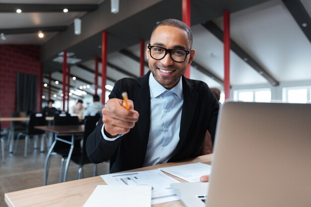 Empresário sorrindo e apontando com o botão no local de trabalho