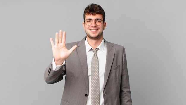 Empresário sorrindo e parecendo amigável, mostrando o número cinco ou quinto com a mão para a frente, em contagem regressiva