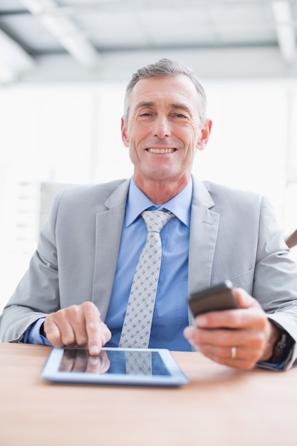 Foto empresário sorrindo para a câmera com o tablet e o telefone dele