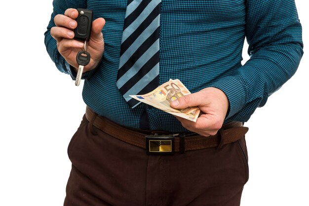Empresario sosteniendo billetes en euros y llaves de coche aisladas en primer plano de la pared blanca. Concepto de compra o alquiler de coche